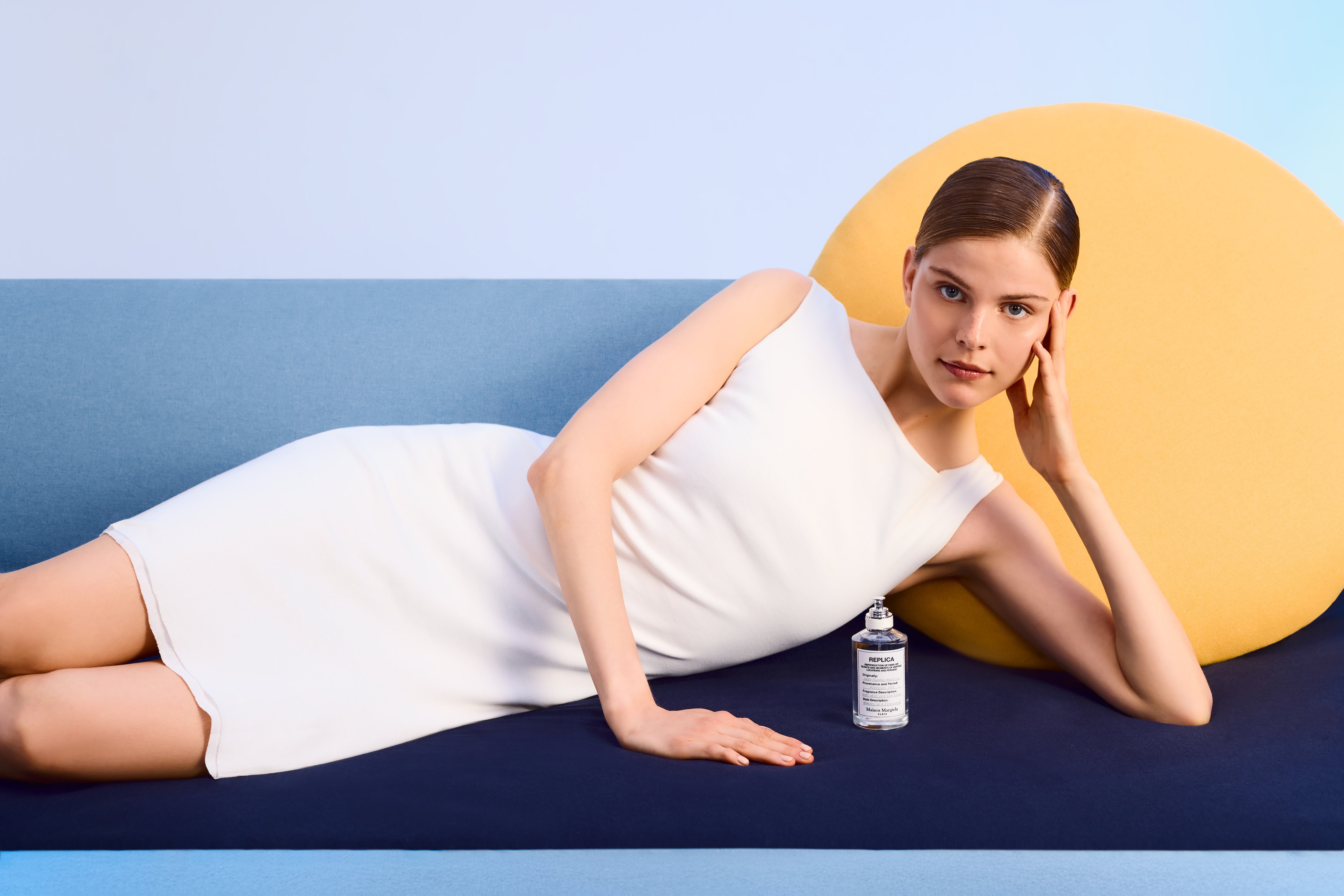 Woman in a white dress lying on a blue surface with a yellow circle in the background